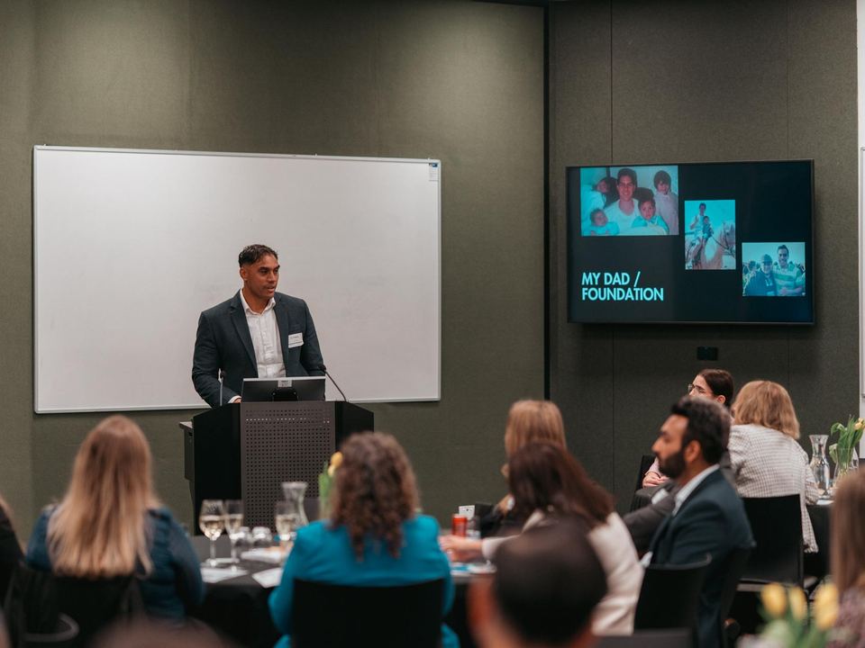 AJ Tuhoro speaking at a lectern to a room of business leaders